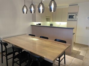 A modern kitchen with a central island, a dining table with chairs, pendant lights, and a built-in microwave. - Apartment Near Marina Nieuwpoort & Golf (Nieuwpoort)