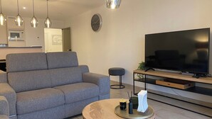 A modern living room with a grey sofa, a round coffee table with a tray, a flat-screen TV, and pendant lights. - Apartment Near Marina Nieuwpoort & Golf (Nieuwpoort)