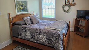 A bedroom with a wooden bed, a large window, a television, and a wall-mounted shelf with a wreath.