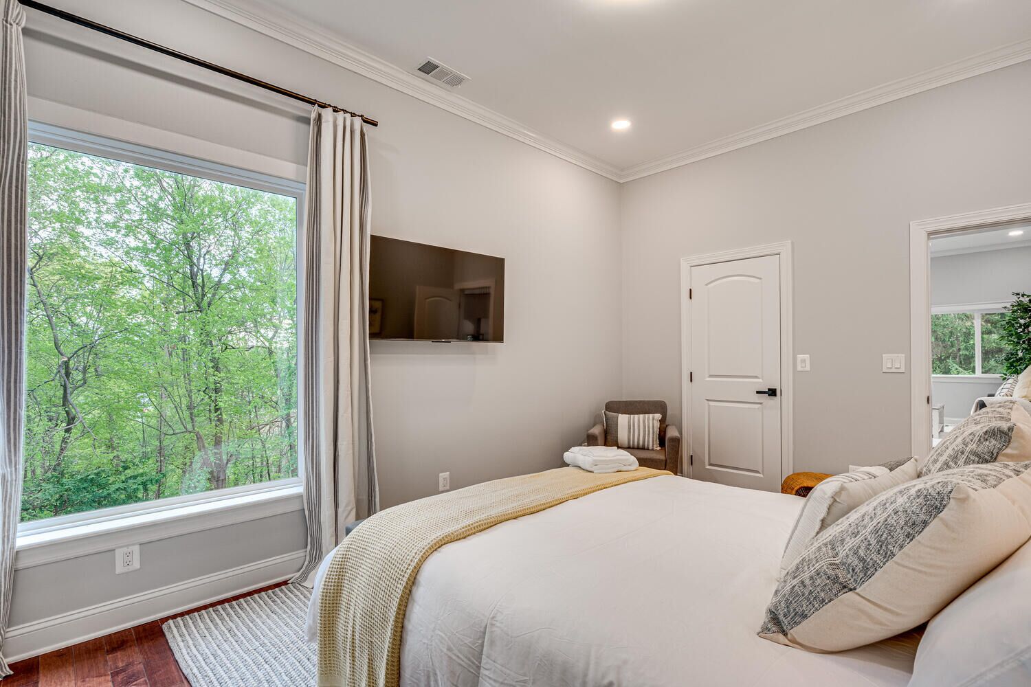 Une chambre avec une grande fenêtre, un lit, une chaise et une porte.