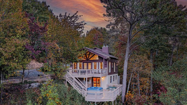 A two-story cabin with a deck and a hot tub, surrounded by dense forest. - Majestic Cabin Getaway • Epic Views, Hot Tub & Game Room • Family-Friendly (Gatlinburg)