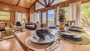 A wooden interior with a dining table set for a meal, a sofa, and a window with a view of the outdoors. - Majestic Cabin Getaway • Epic Views, Hot Tub & Game Room • Family-Friendly (Gatlinburg)