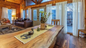 A cozy cabin interior with a wooden dining table, a sofa, and a large window with curtains. - Majestic Cabin Getaway • Epic Views, Hot Tub & Game Room • Family-Friendly (Gatlinburg)