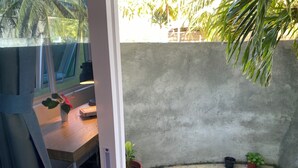 A small, enclosed outdoor space with a concrete wall, a tiled floor, and a wooden table with a potted plant. - Calm Beach Inn (Gan)