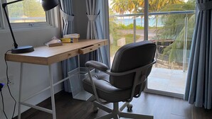 A modern office space with a desk, chair, and large window with curtains. - Calm Beach Inn (Gan)