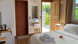 A hotel room with a bed, a wooden desk, a small stool, a mirror, a door leading to a balcony, and a window with curtains. - Calm Beach Inn (Gan)