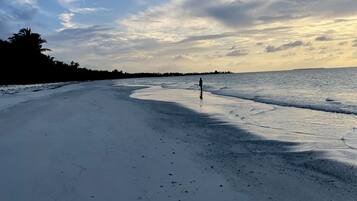 A beach with a person standing in the distance, a clear sky, and calm sea.