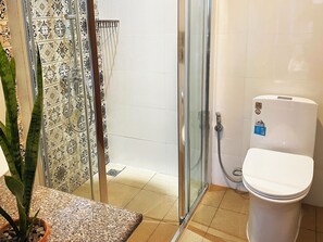 A bathroom with a glass shower enclosure, a toilet, and a potted plant.
