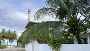 A coastal building with a white exterior, palm trees, and a red communication tower in the background. - Calm Beach Inn (Gan)