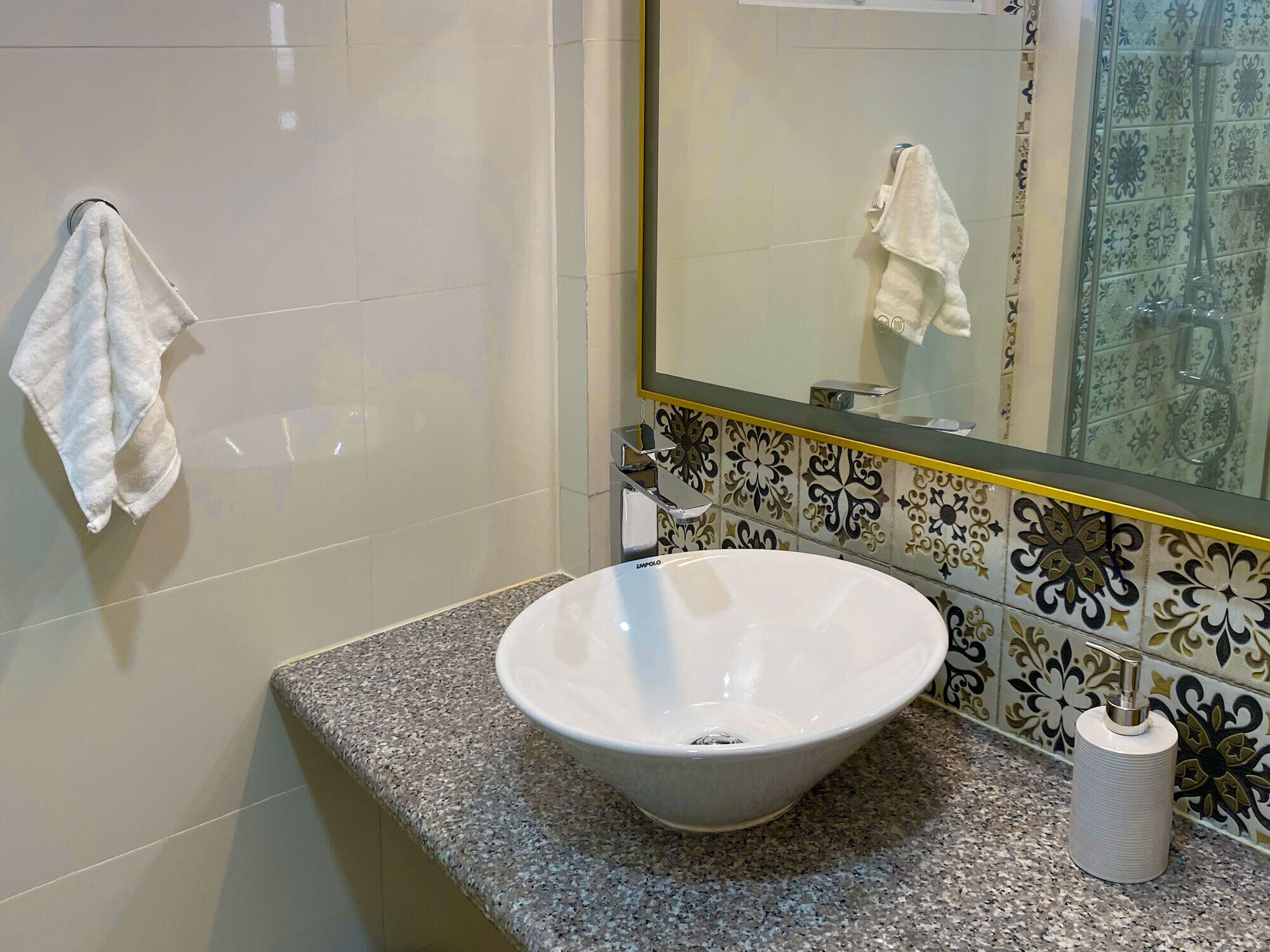 Un bagno con un lavandino bianco, uno specchio e un asciugamano appeso al muro.
