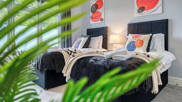A modern bedroom with a large bed, two bedside tables, and abstract wall art. - Stunning 6 bed in Nottingham - Sleeps 16 (Nottingham)