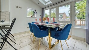 A dining area with a table set for four, blue chairs, and a view of the outside through large windows. - Stunning 6 bed in Nottingham - Sleeps 16 (Nottingham)