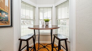 Habitación de esquina con una mesa redonda y dos taburetes, una planta en maceta y un cuadro en la pared.