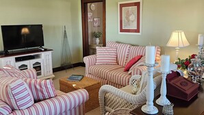 A living room with striped sofas, a television, a small table with candles, and a decorative basket.