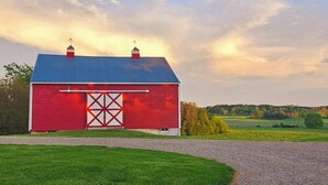 A red barn with a white door and a blue roof, surrounded by green fields and a cloudy sky.