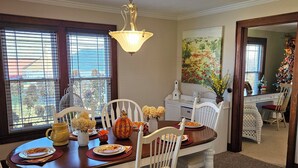 A dining area with a wooden table set for four, white chairs, and a hanging light fixture.