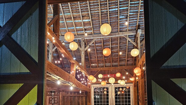 A rustic wooden interior with a wooden bench and picnic table, string lights, and paper lanterns.
