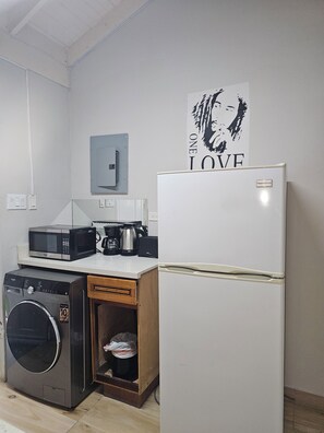 A compact kitchen with a washing machine, microwave, coffee maker, and a refrigerator.