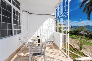 A balcony with a table and chairs, a view of the sea, and a thatched-roof structure in the background. - Cozy Seaview studio in Montego Bay with AC (Montego Bay)