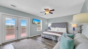 A bedroom with a bed, a ceiling fan, a nightstand, a lamp, and a view through the window.