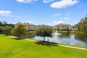 A residential complex with multiple apartment buildings, a central pond with a fountain, and a well-maintained lawn.