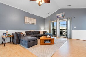 A spacious living room with a sectional sofa, a wooden coffee table, and a large window offering a view.