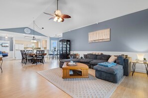 Uma sala de estar ampla com um sofá grande, uma mesa de centro e um espaço de jantar com cadeiras e uma mesa.