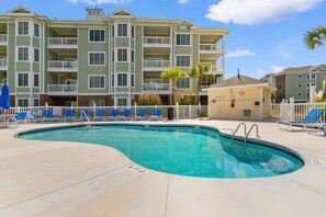 A swimming pool with a lifeguard stand, lounge chairs, and a building with balconies in the background.