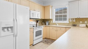 A kitchen with white appliances, wooden cabinets, a window with blinds, and a countertop with a coffee maker. - Water Views- 5 Beds- Near Broadway @ Beach- Pools (Myrtle Beach)