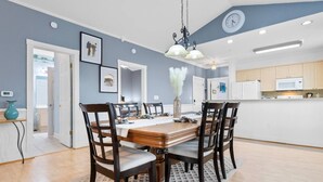 A dining area with a wooden table and chairs, a chandelier, and a kitchen in the background. - Water Views- 5 Beds- Near Broadway @ Beach- Pools (Myrtle Beach)