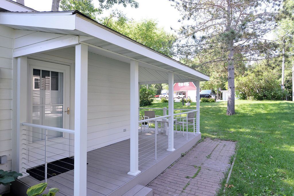 Ein eingeschossiges Haus mit überdachter Veranda, Eingangstür und kleinem Vorgarten mit Rasenfläche und Baum.