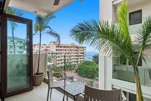 A balcony with a glass door, a potted plant, a chair, and a view of a building complex.