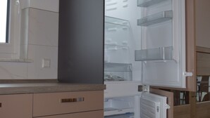 A compact kitchen with a built-in refrigerator, a window, and wooden cabinets. - Hunsr./Reich vacation apartment in the countryside suitable for family a. fitter (Reich)