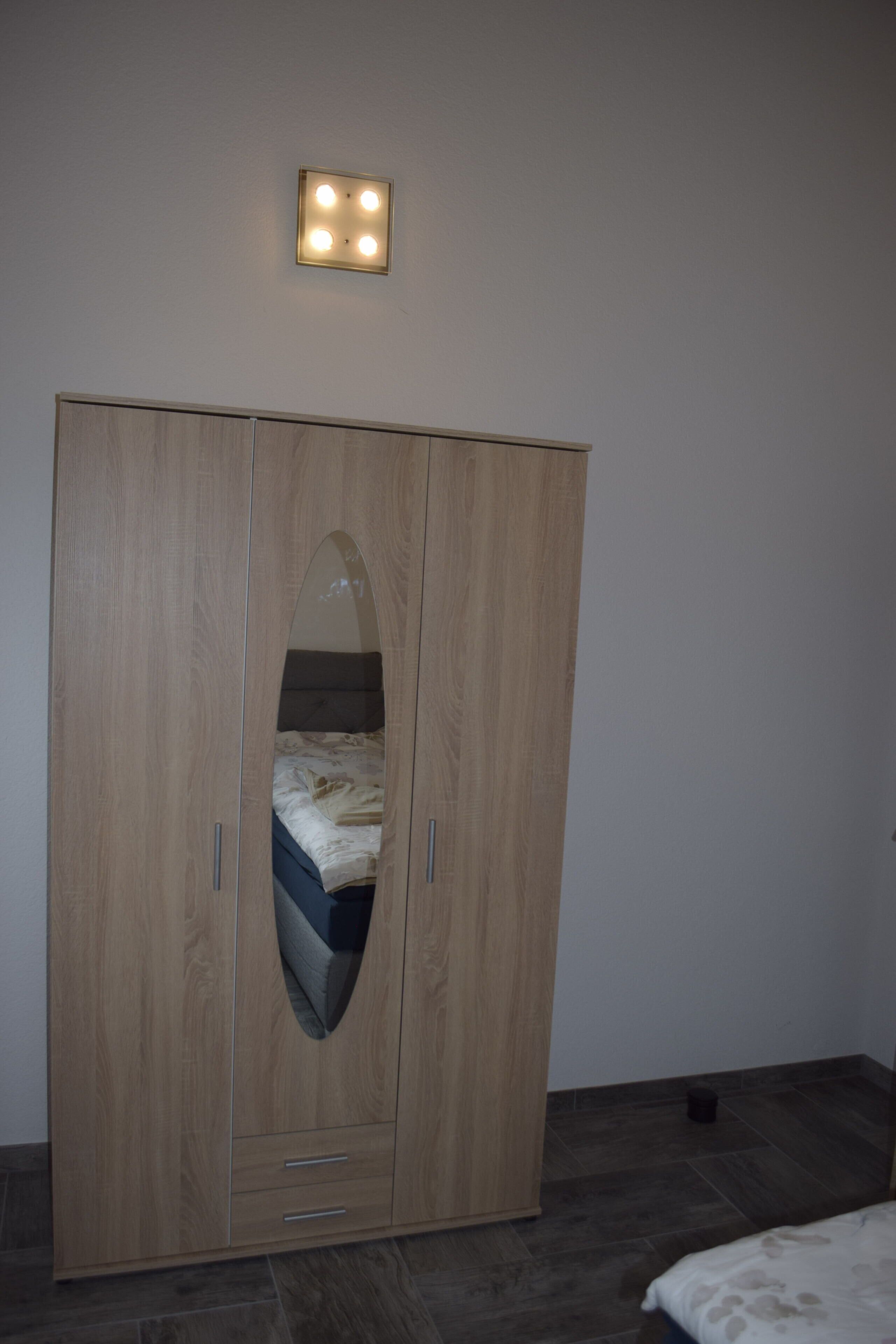 Una camera da letto con un armadio in legno, un letto con copriletto decorato e una lampada a parete.