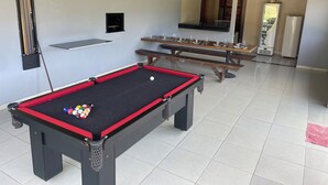 Een pooltafel met ballen, een biljartrek en een hanglamp in een ruimte met betegelde vloer en een bank.