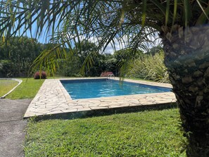 A rectangular swimming pool with a stone border, surrounded by well-maintained grass and palm trees. - Inn with a Pool and Lake (Quatro Barras)