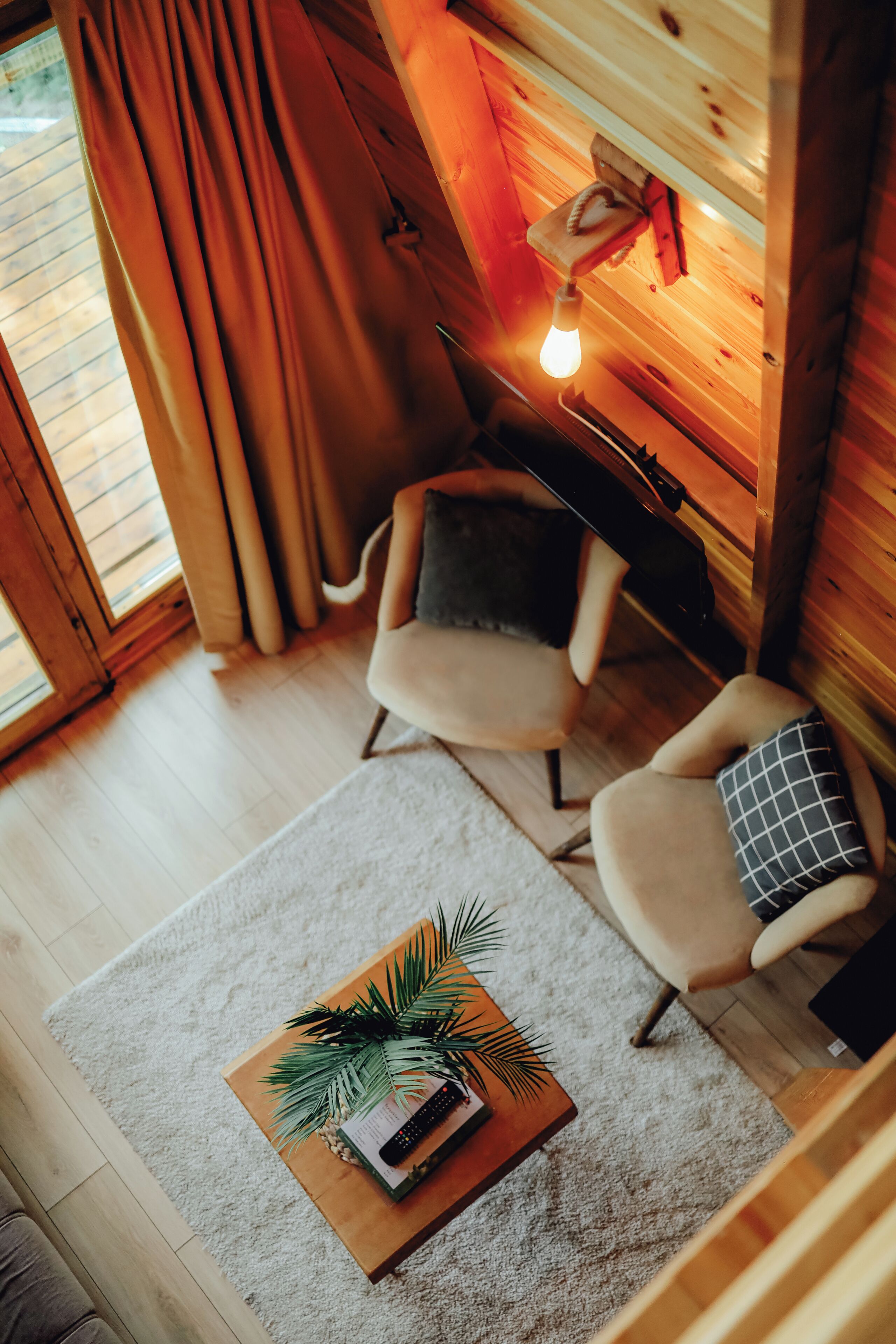 A cozy room with a wooden interior, a comfortable chair, a small table with a plant, and a hanging light fixture.