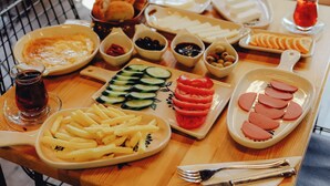 A table with various food items and utensils, including plates of sliced cucumbers, tomatoes, and meat, as well as a bowl of olives and a glass of red drink. - Natural Life Bungalows Sapanca (Sapanca)