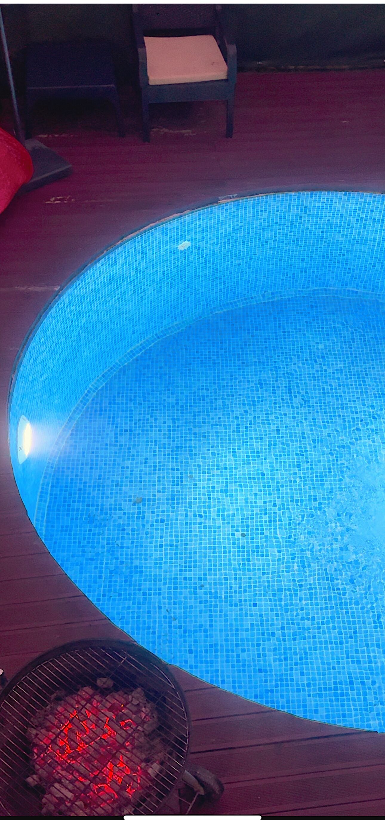 A swimming pool with a tiled edge and a grill with red coals.