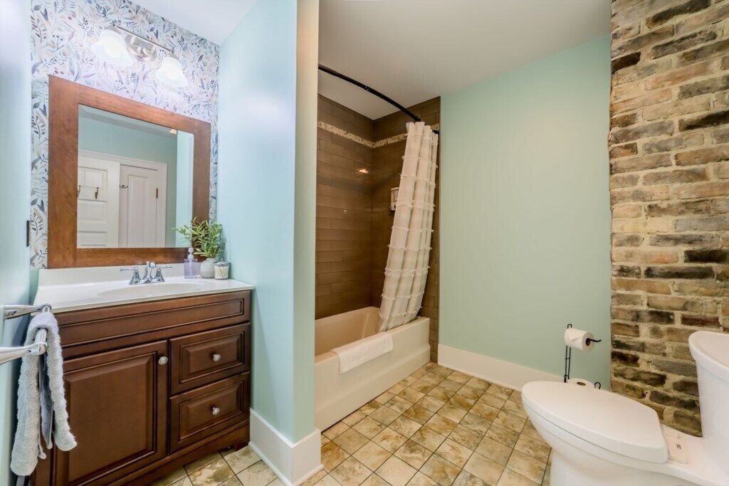 Une salle de bain avec un meuble-lavabo en bois, une douche avec un rideau, des toilettes et un mur en briques.