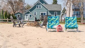 A beach with two blue beach chairs, a wooden bench, and a stone fire pit. - State Ave|Beach|King Beds|Central AC (Alpena)