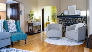 A living room with a stone fireplace, teal and gray armchairs, wooden flooring, and a white rug. - State Ave|Beach|King Beds|Central AC (Alpena)