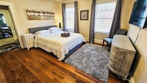A bedroom with a bed, bedside tables, a TV, and a window with curtains. - The Terrace (Charlotte)