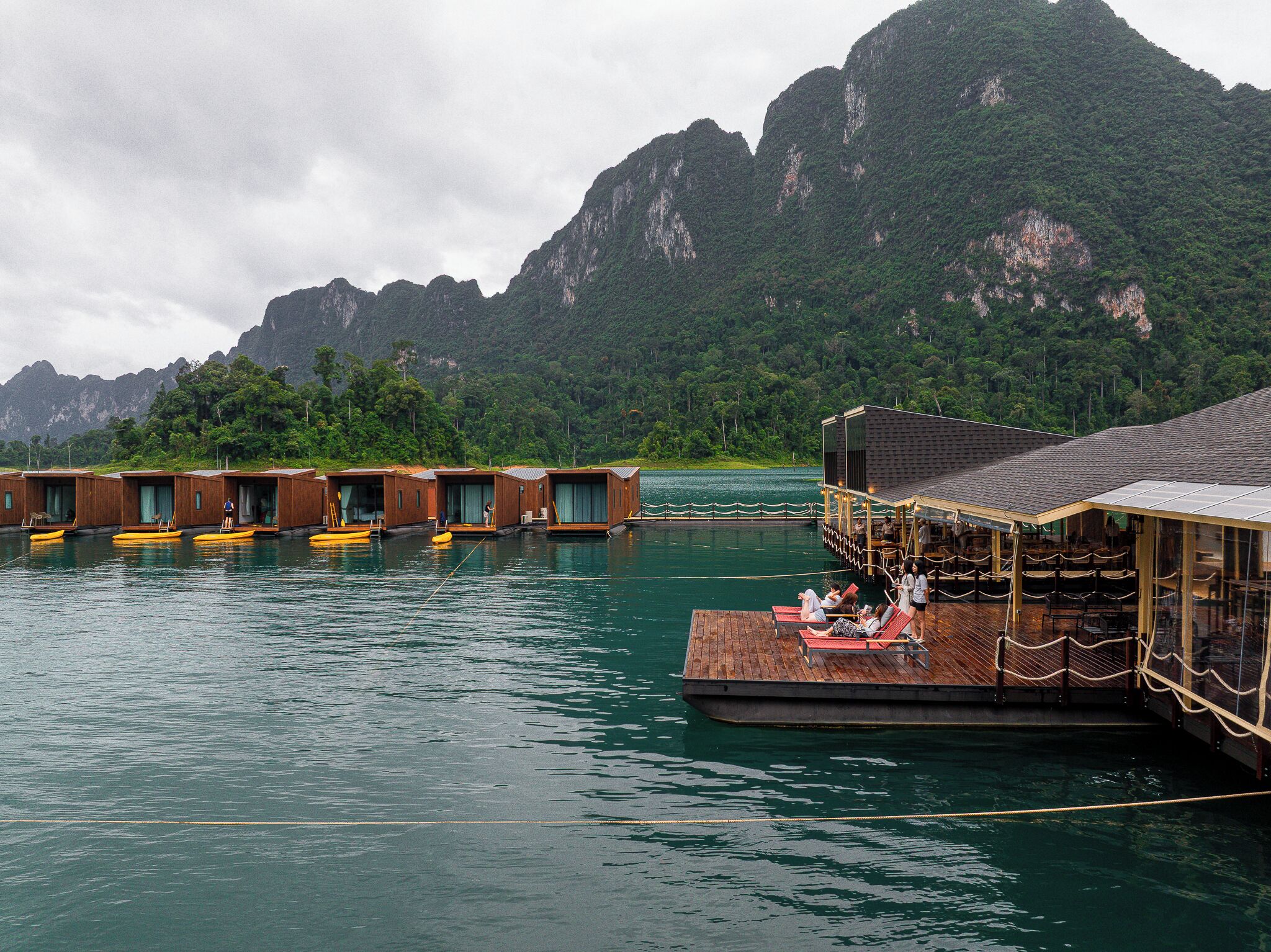 Structures flottantes en bois, à ciel ouvert, comprenant un espace repas avec tables et chaises, et offrant une vue sur un paysage montagneux.
