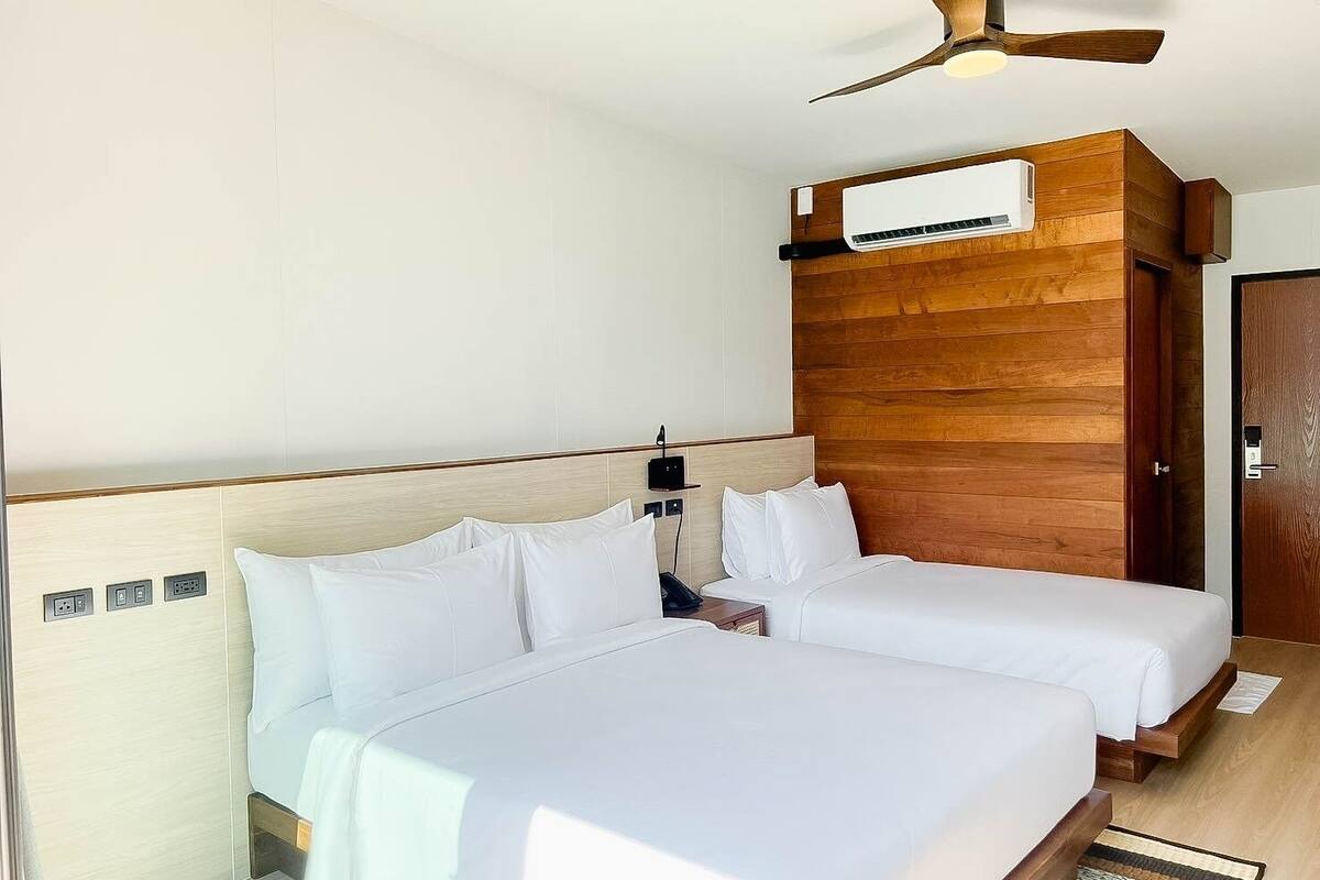 A hotel room with two beds, a ceiling fan, an air conditioning unit, and a wooden accent wall.