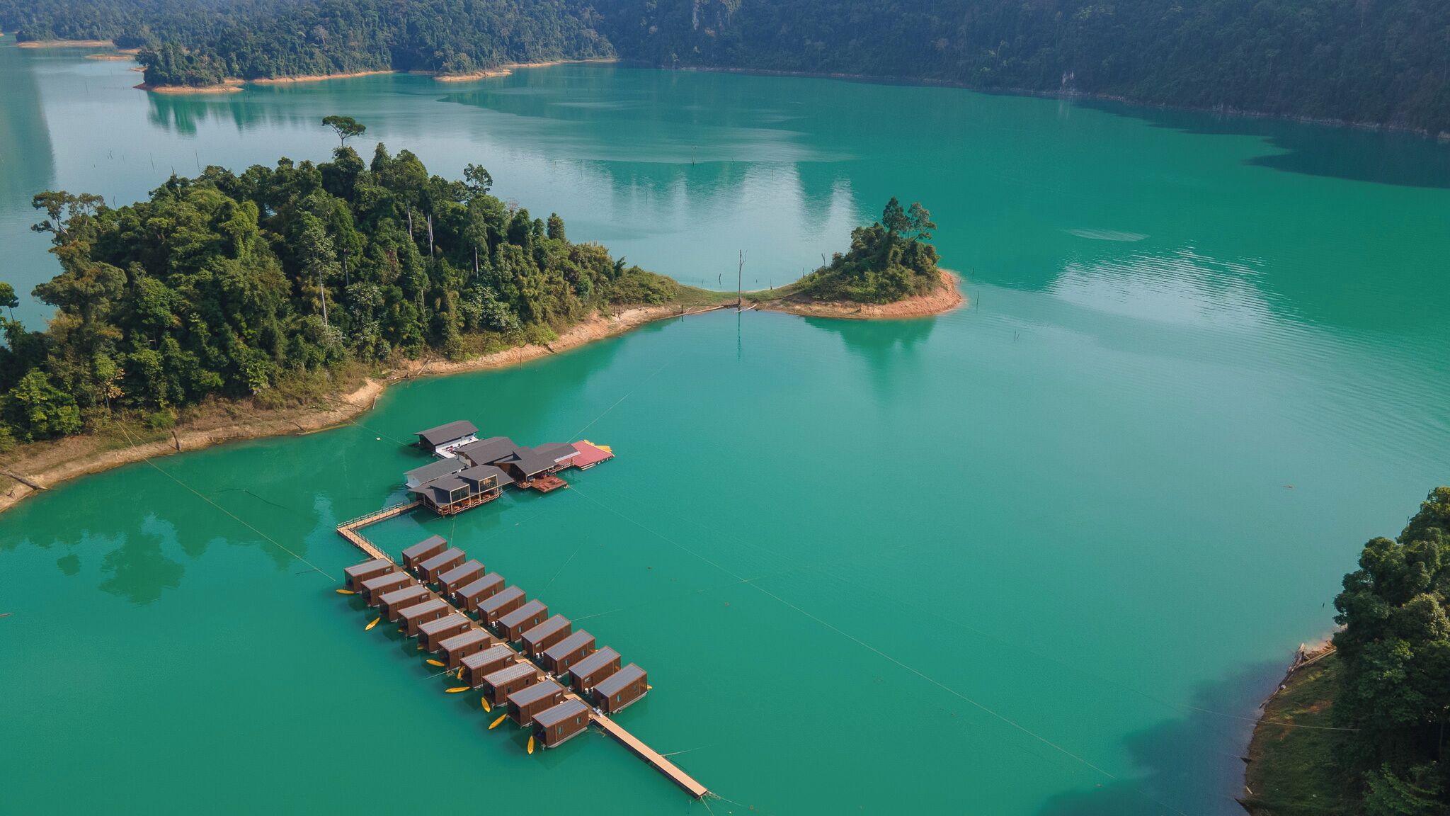 An aerial view of a lakeside property with a dock extending into the water, surrounded by dense forest.