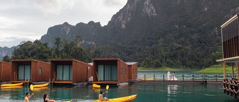 Un plan d’eau agrémenté de structures flottantes en bois, de kayaks, et dominé par un paysage montagneux.