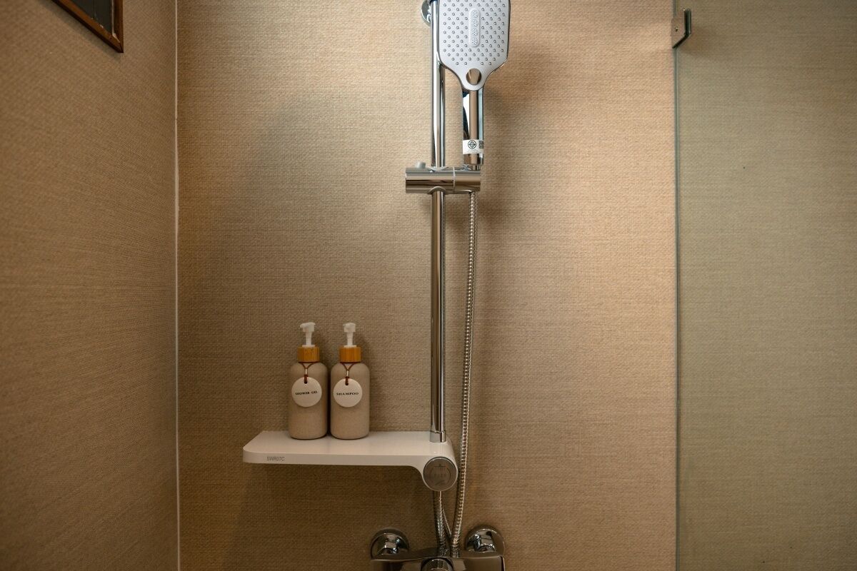 A bathroom with a shower, a shelf with two bottles of shampoo, and a towel rack.