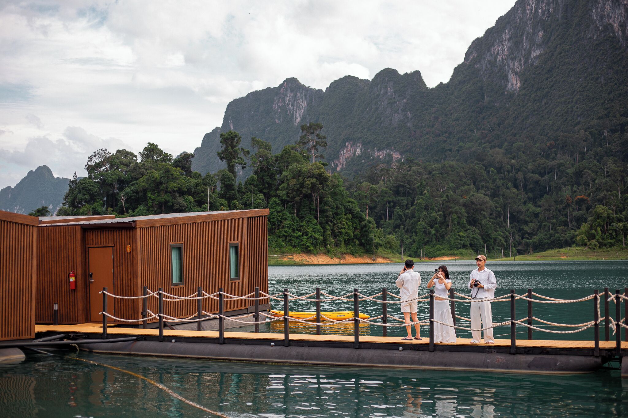 A wooden dock with a small building, a yellow boat, and a lake with mountains in the background.