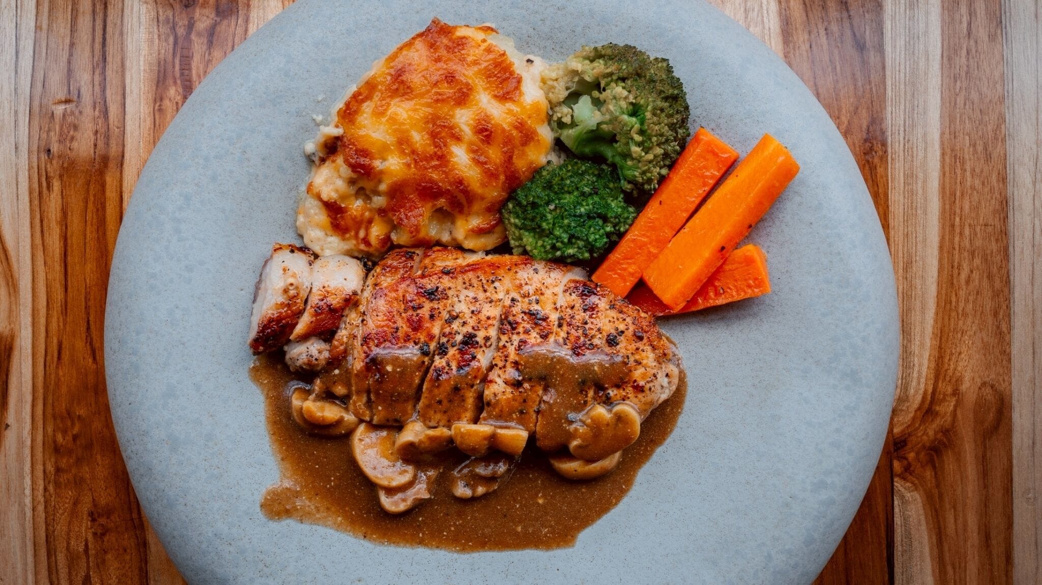 A plate of food with a piece of meat, mashed potatoes, broccoli, and carrots.